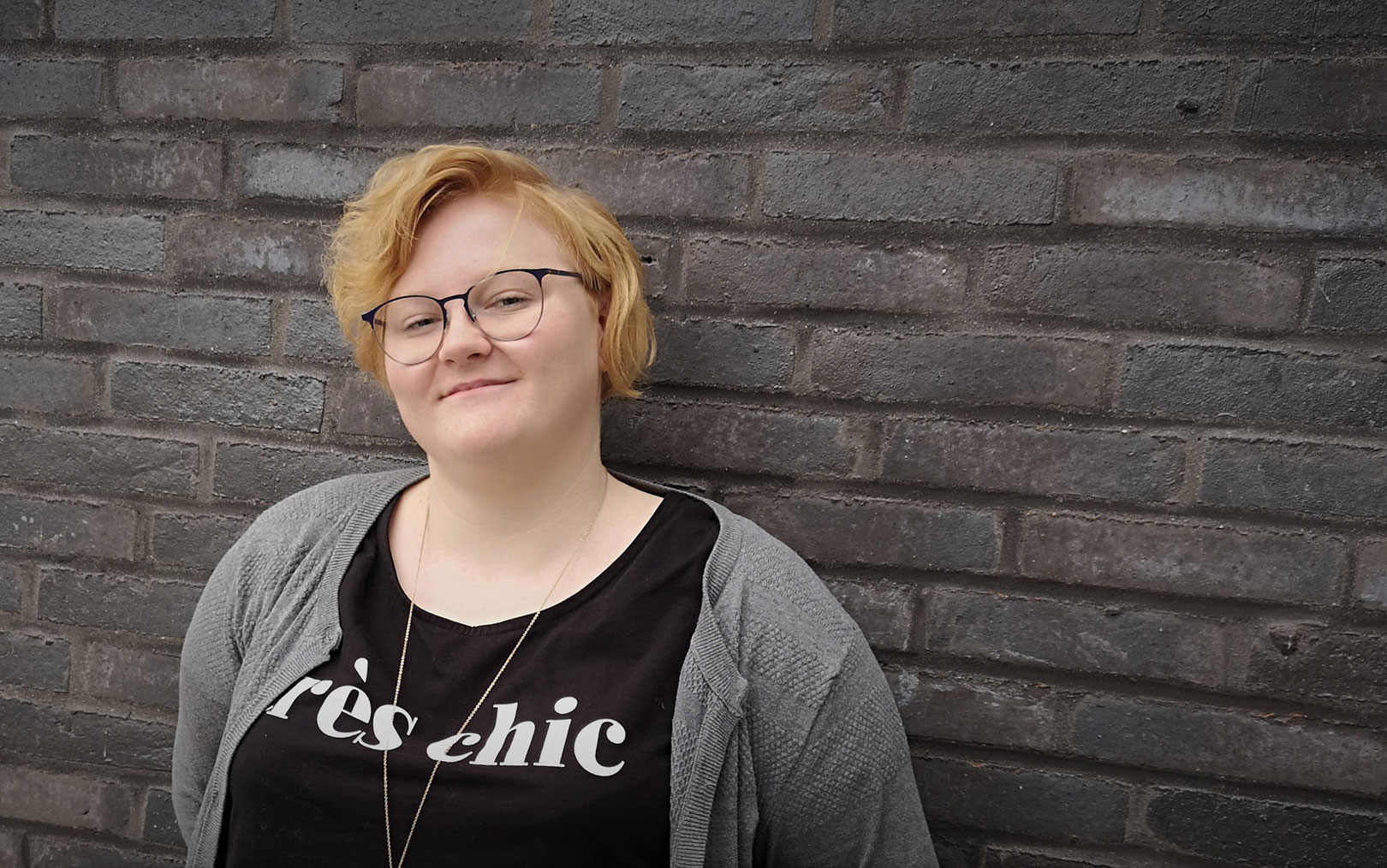 Serviceøkonom Emma Rasmussen kigger på dig med hovedet lidt på skrå op ad sort murstensvælg