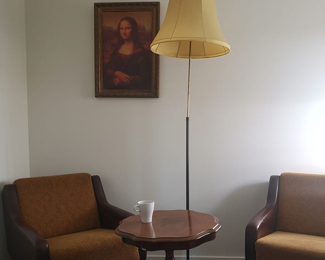 To brune lænestole med et rundt sofabord mellem sig, en høj lampe og et maleri af Mona Lisa i baggrunden
