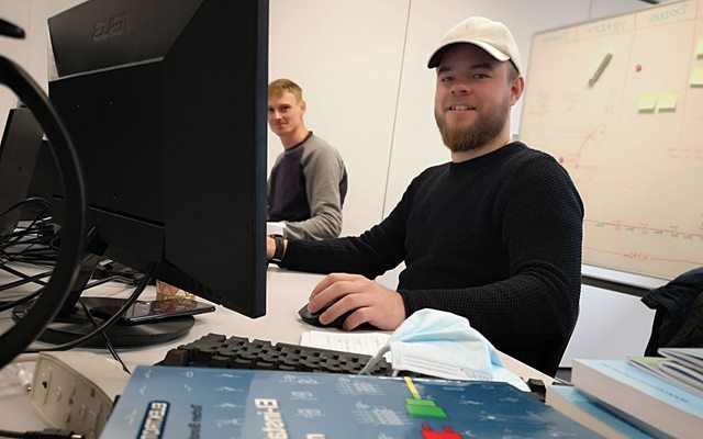 El-installatør Studerende Thomas Doktor sidder ved sin computer med bg foran sig og kigger smilende på dig