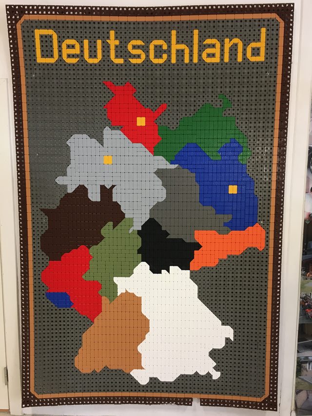 Et rektangulært stykke skridsikkert gulv i grå plast med et flerfarvet kort over Tyskland som motiv og påskriften 'Deutschland'.