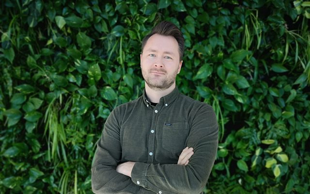 Klaus Mogensen, der har været på bestyrelsesuddannelse på Erhvervsakademi Dania, står foran grøn platevæg med armene over kors i grøn skjorte og ser på dig