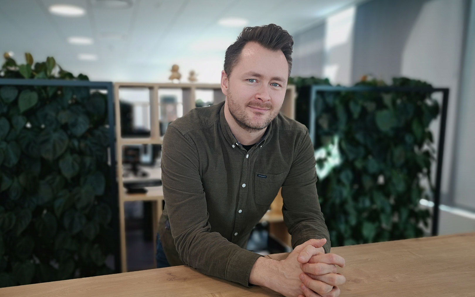 Klaus Mogensen, der har været på bestyrelsesuddannelse på Erhvervsakademi Dania, smiler til dig foroverbøjet ved skrivebord med foldede hænder