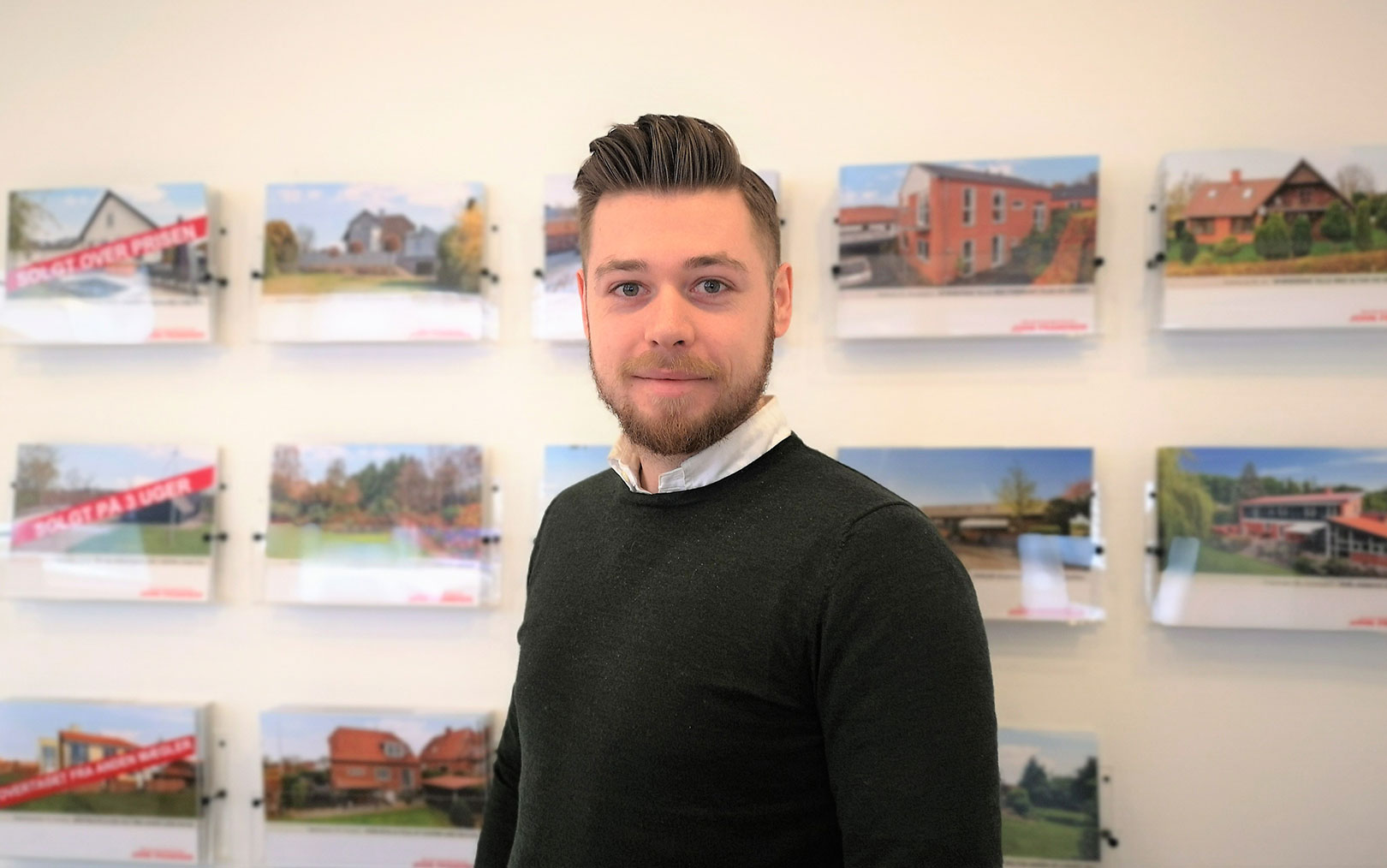 Danny Hedegaard, finansøkonom fra Erhvervsakademi Dania, smiler til dig foran en række salgsopstillinger på kontoret i Horsens