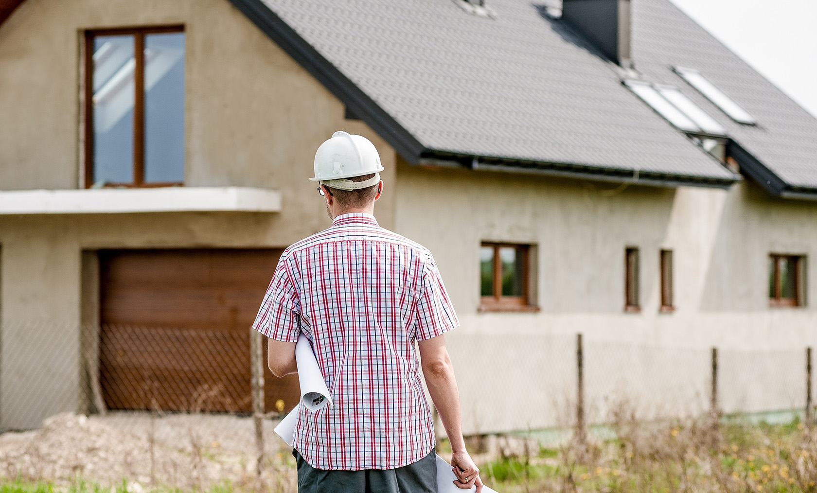 Mand går foran hus med tegninger under armen og sikkerhedshjelm på hovedet