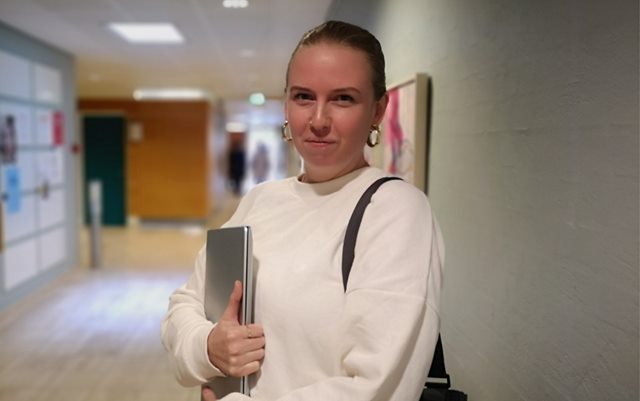 Kathrine Fæer, handelsøkonom studerende, står på gangen med sin computer under armen