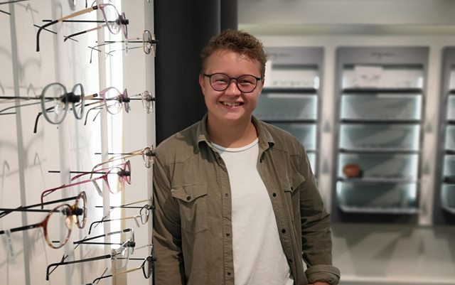 Optometri studerende Jens Munch smiler på sit praktiksted, hvor man ser briller i forgrunden