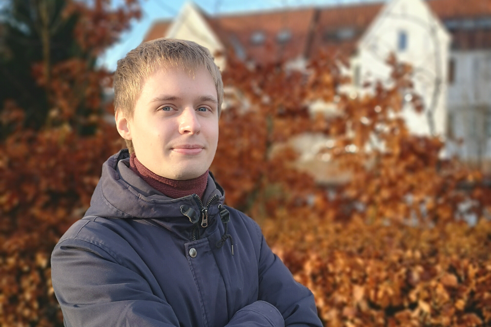 Datamatiker Filip Grønkjær Jensen står med armene over kors udenfor med jakke på foran en brun bøgehæk