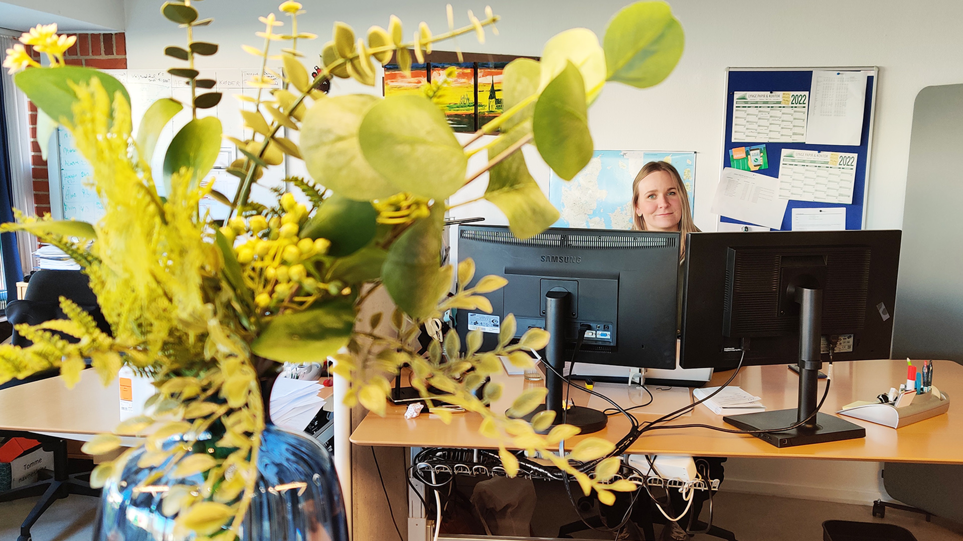 Camilla Østerdal ved computeren i baggrund, mens blomster er i forgrunden