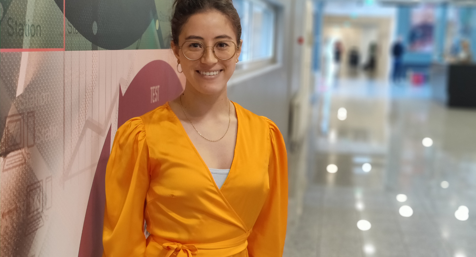 Nyuddannet optometrist Nina Nilsson står i sin orange kjole på gangen på Erhvervsakademi Dania