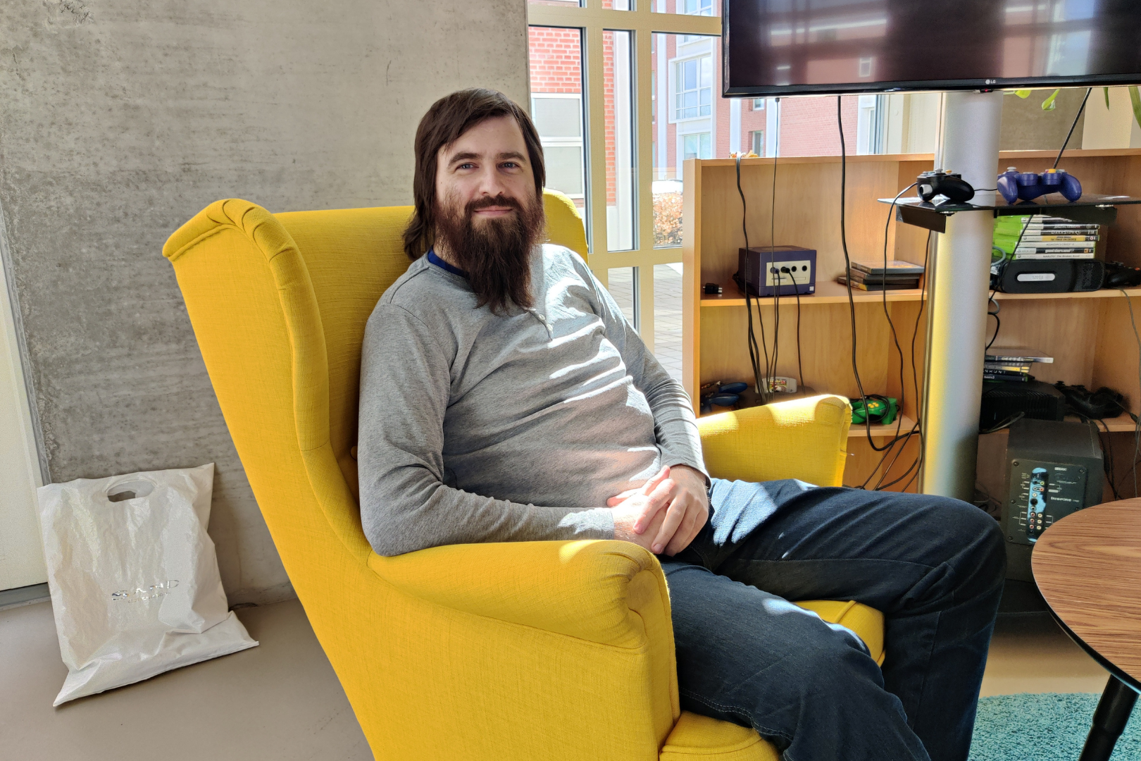 Kasper Fly, der læser på Erhvervsakademi Dania i Grenaa, sidder i en gul lænestol med hænderne foldet i skødet og en masse spilconsoller i baggrunden