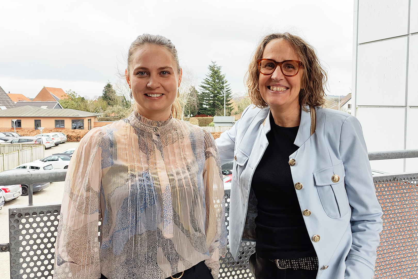 Bankrådgiverne Maria og Karen på svalegangen med horisont og grantræ i baggrunden