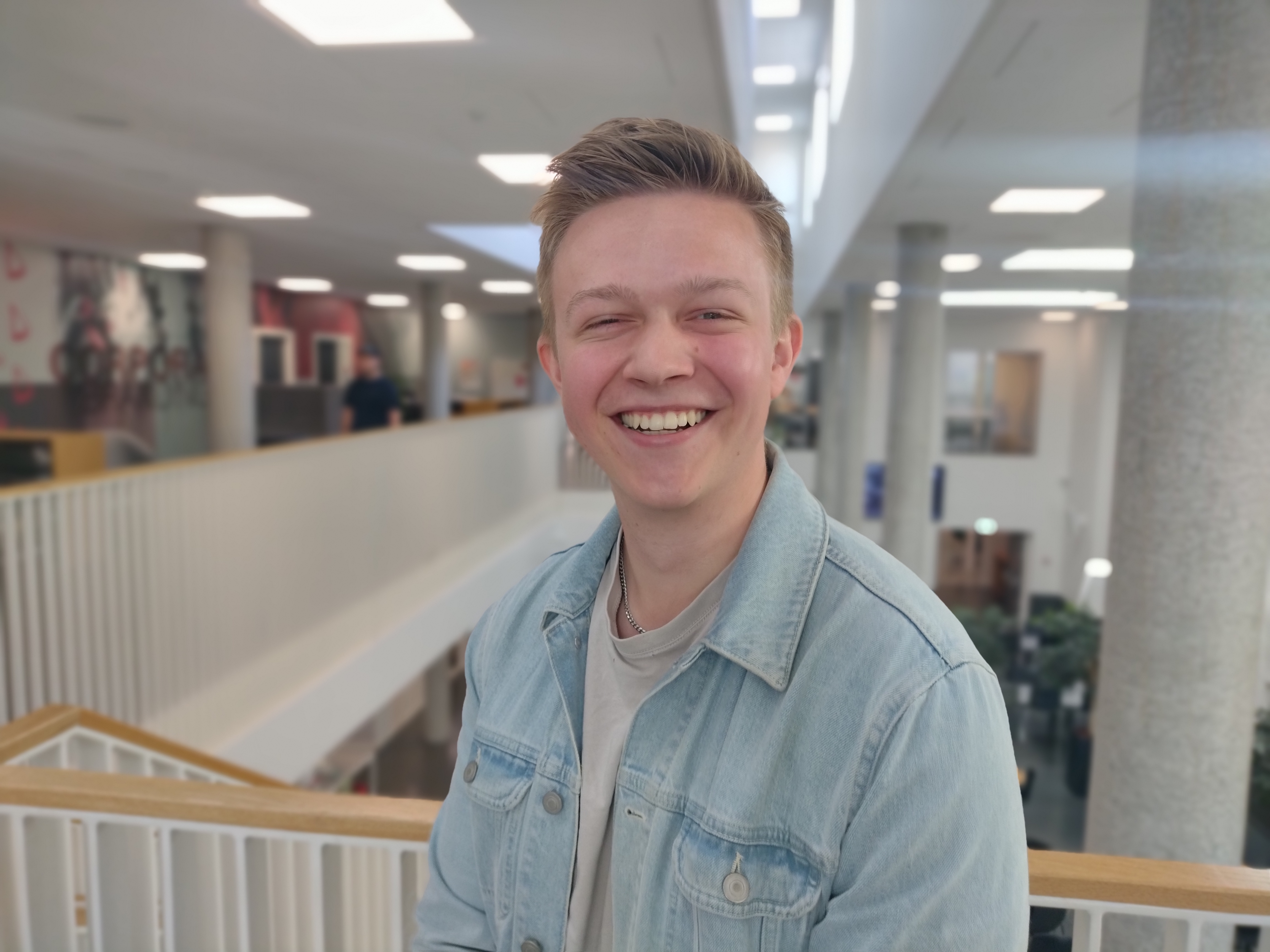 Oliver, der læser til markedsføringsøkonom, smiler med kantinen på Erhvervsakademi Dania i Randers som baggrund