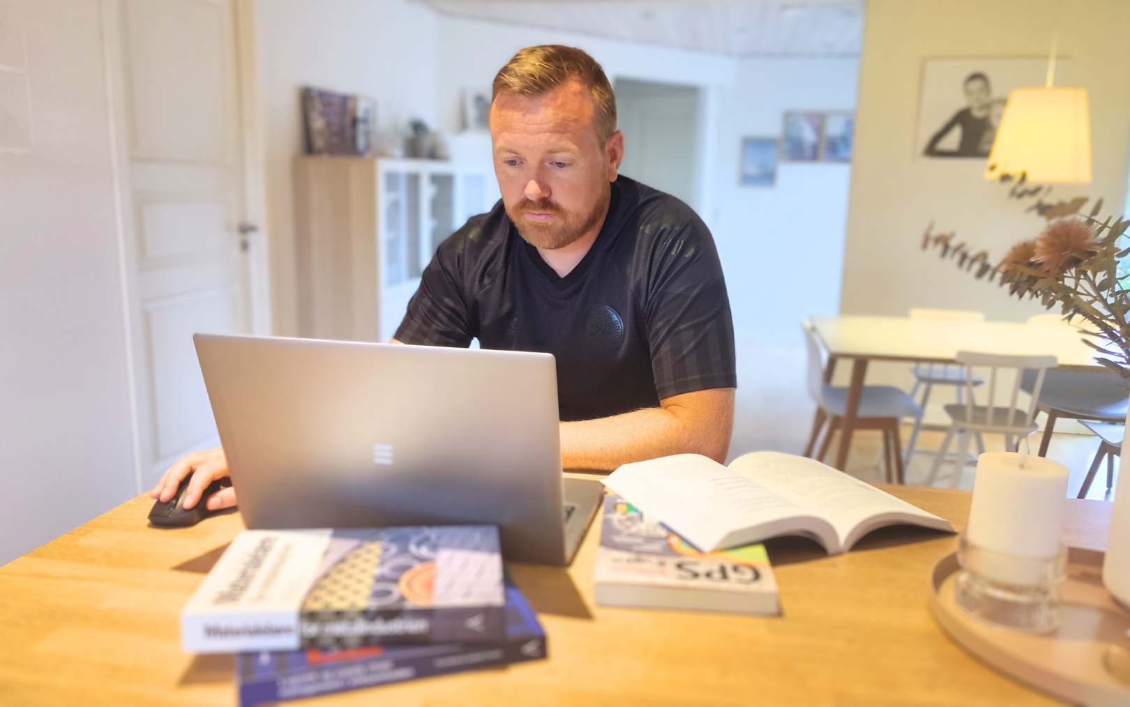 Brian, der læser til produktionsteknolog på Erhvervsakademi Dania i Randers, sidder ved sin computer ved køkkenbordet og arbejder, mens bøger til studiet ligger rundt om ham 