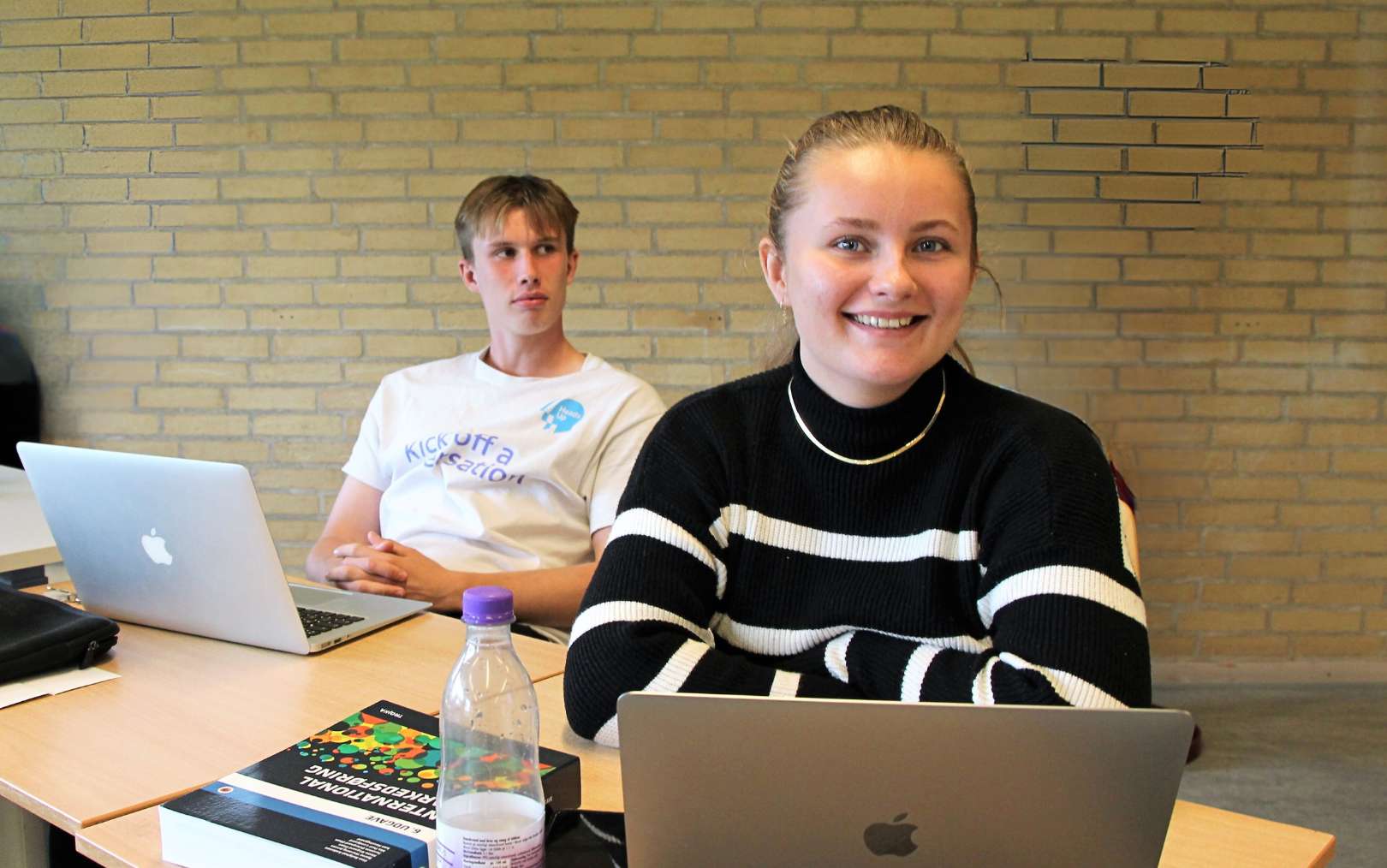 En pige sidder ved sin computer med en dreng ved siden af sig lidt bagud på Erhvervsakademi Dania i Hobro