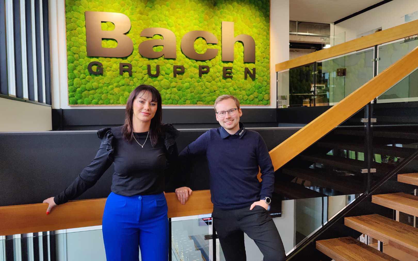 Camilla og Peter står foran et grønt skilt med Bach Gruppens logo, da de er i finalen som Erhvervsakademi Danias bedste praktikophold