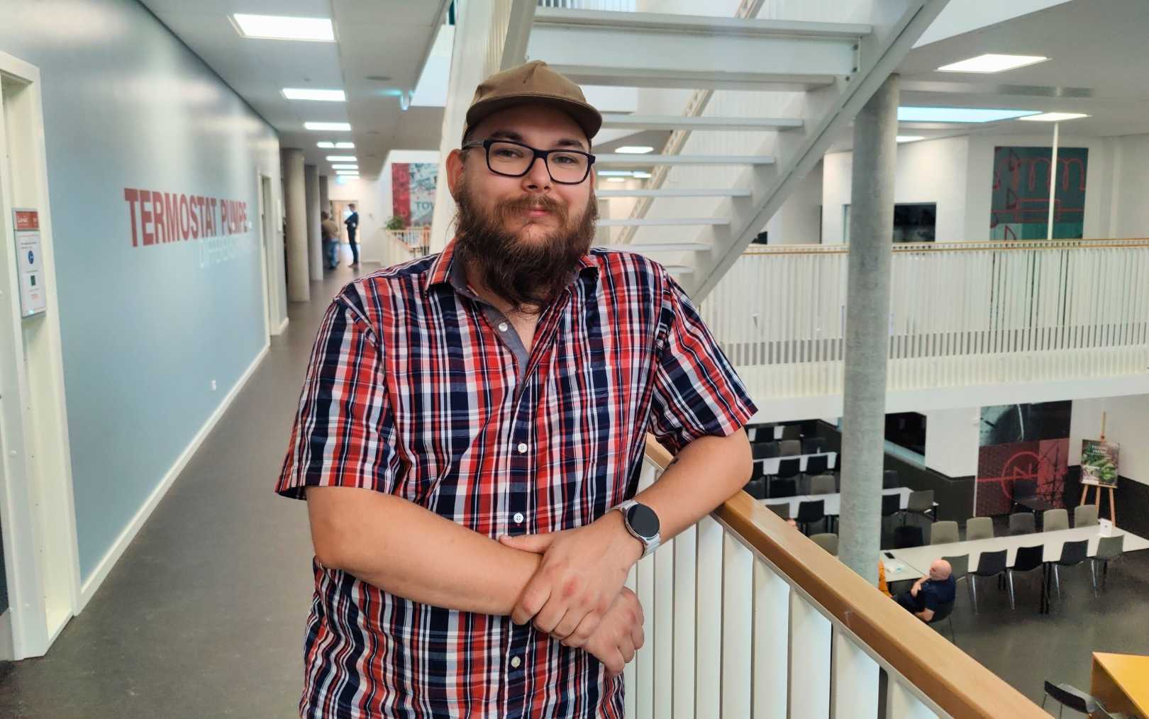 Johannes Mai læser til produktionsteknolog på Erhvervsakademi Dania i Randers, hvor han står med den ene arm på rækværket i kantineområdet